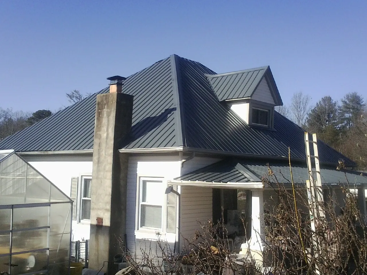 Dark blue standing seam metal roof on a white farmhouse with dormer — Slate & Tile Roof Repair by Roofing Brothers in Piermont