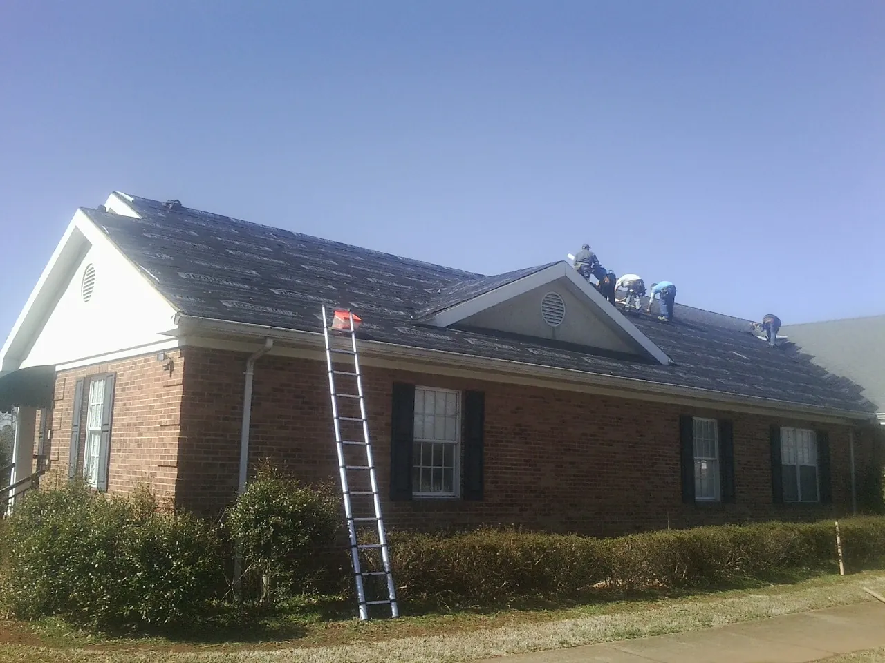 Crew tearing shingles off a brick ranch roof with a ladder set — Metal Roof Repair work by our crew in Piermont