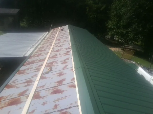 Old rusted panels beside newly installed green metal roofing — Wind Damage Roof Repair by Roofing Brothers in Piermont