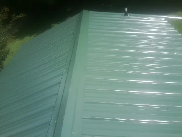 New green metal panels meeting at the ridge of a roof — Flat Roof Repair work by our crew in Piermont