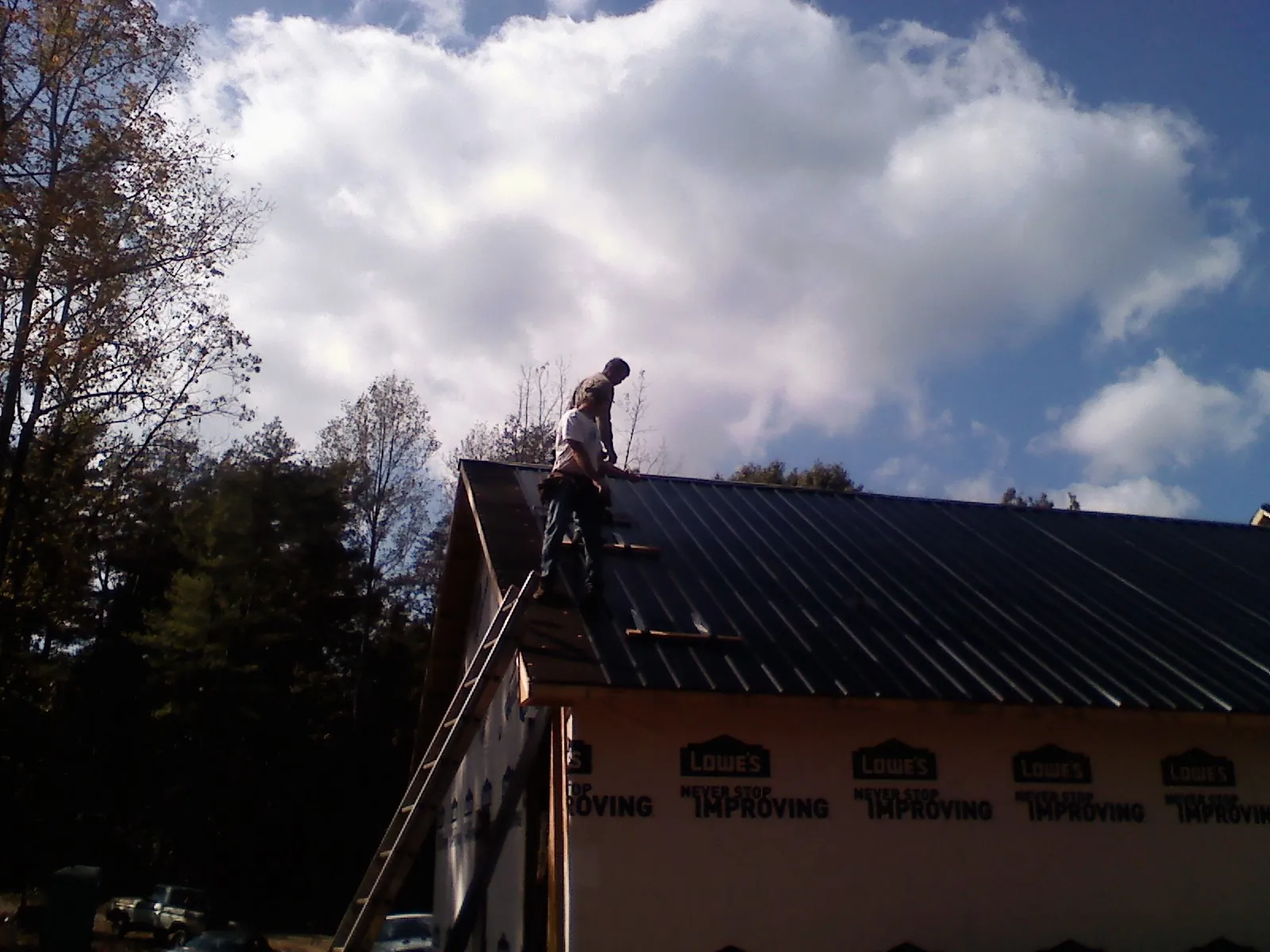 Roofer fastening dark metal panels high against a cloudy sky, from a Roof Inspection job in Piermont