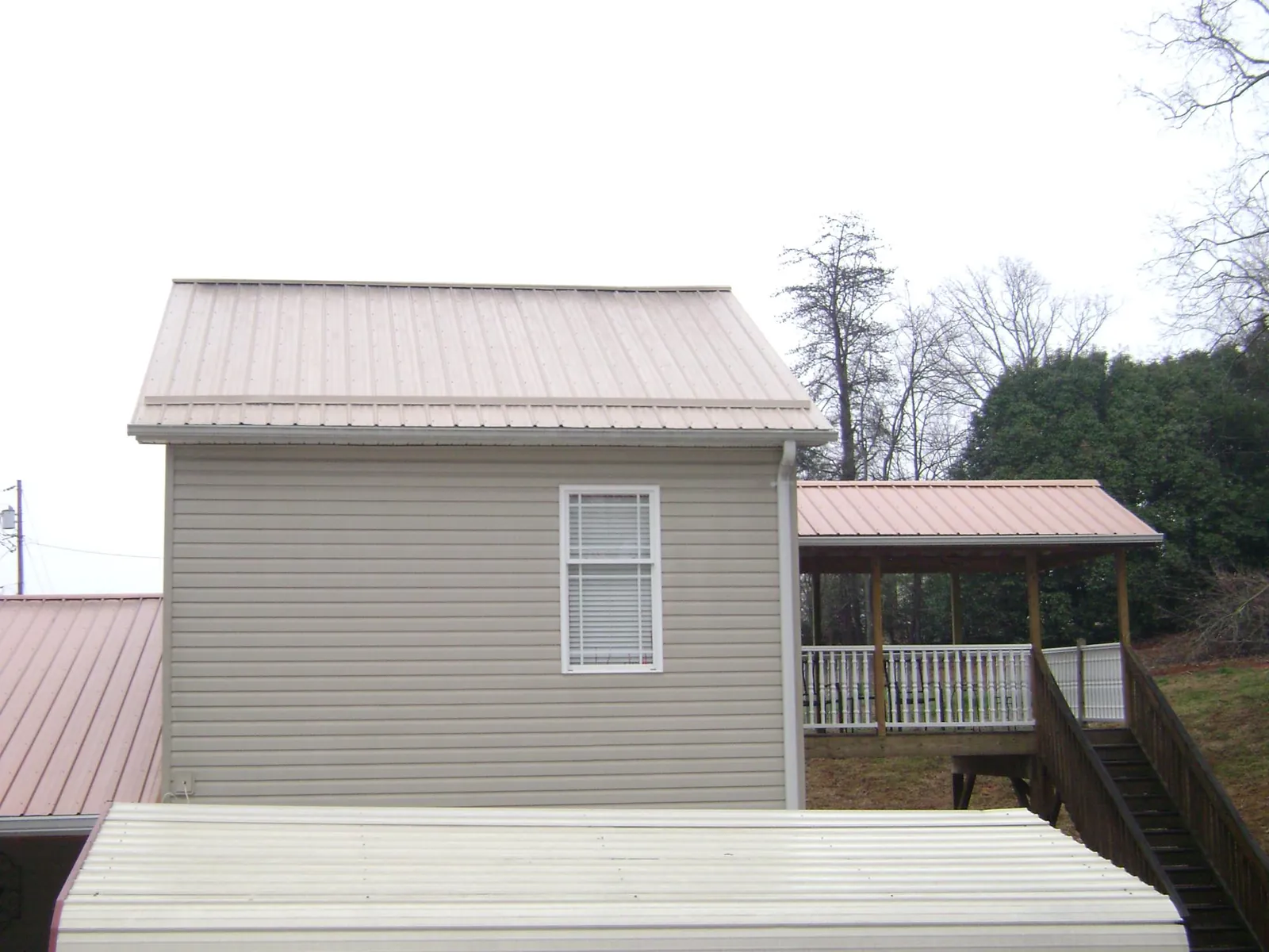 Tan metal roofs on a two story addition and attached porch, from a Roof Replacement job in Piermont